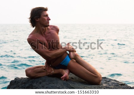 Young man doing yoga exercise on the deserted wild stone sea beach