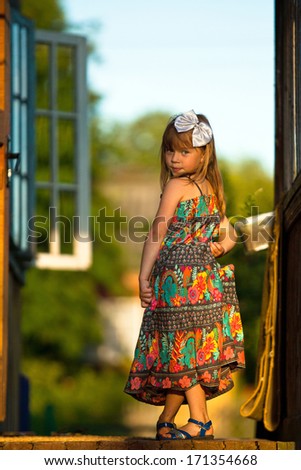 Beautiful little five-year girl posing for the camera on the porch of a village house at sunset