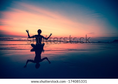 Yoga woman sitting on sea coast at surreal sunset.