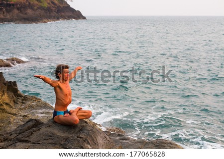 Young man doing yoga exercise on the deserted wild stone sea beach.