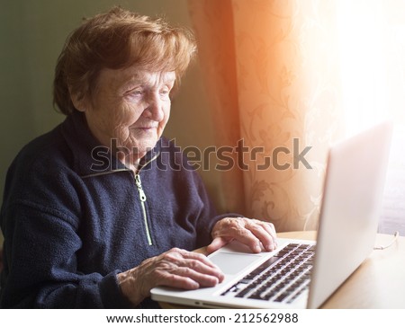 Old woman sing laptop computer at home.