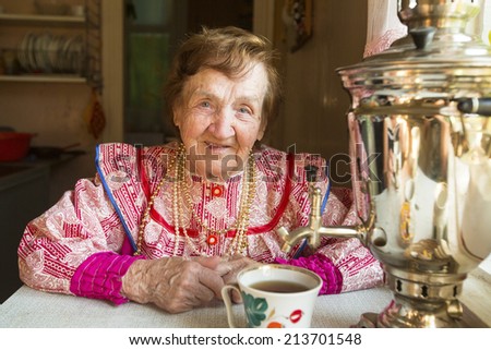 Old woman in ethnic clothes drinking tea in his house.