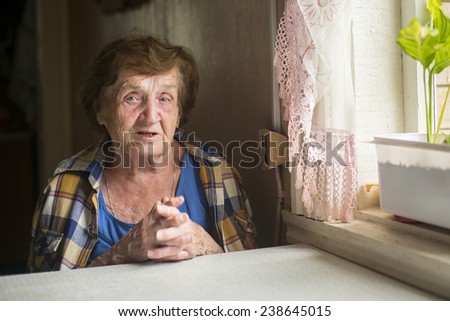 Old woman alone near a window in his country house.
