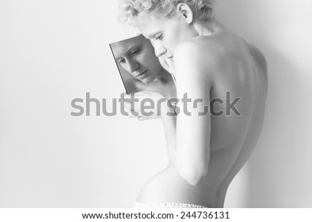 Young sexy lady holding in her hands and looked in the small mirror. Black and white photography in bright colours.