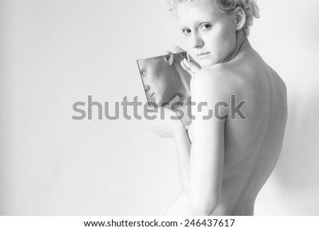 Young sexy lady holding mirror in her hands and looked in the camera. Black and white photography in bright colours.