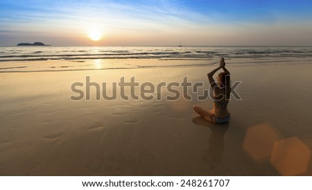 Yoga woman sitting in lotus pose on the beach during amazing sunset. Harmony.