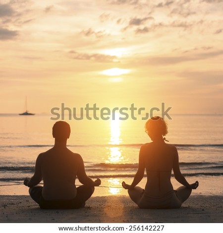 Young couple practicing yoga on Sea beach during sunset.