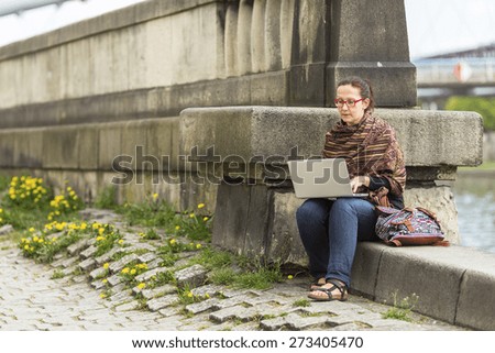 Young woman working on laptop while sitting near the river promenade in the old town.
