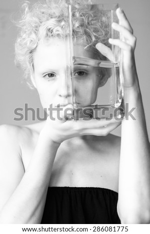 Beautiful girl looks through the empty glass. Black and white photography.