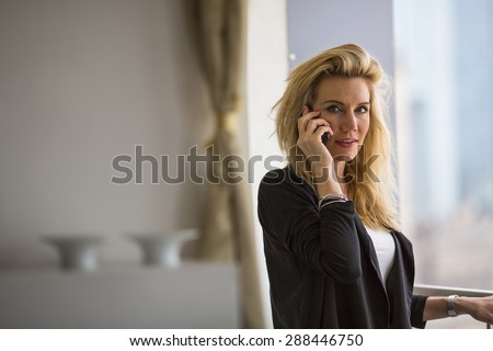 Young blonde business woman talking on the phone while standing on the balcony of the office.