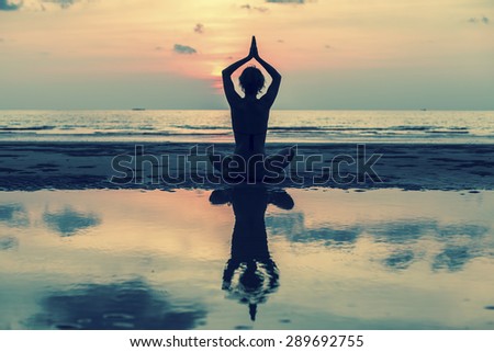 Silhouette of yoga woman sitting in lotus pose on the beach with reflection in water.