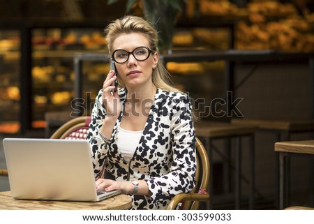 Young woman sitting with laptop in cafe, talking on a cell phone.