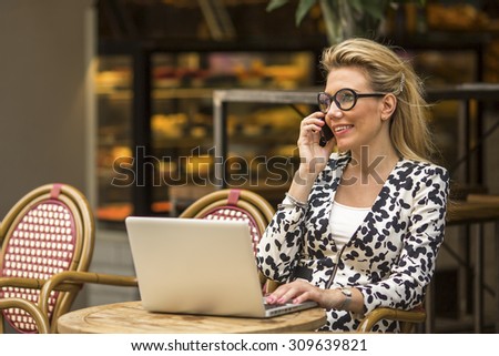Happy business woman talking on the phone and using laptop computer in a coffee shop. Modern business woman.