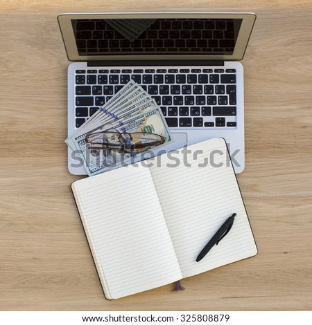 Laptop, dollars bills, and an open notebook with space for your text.
