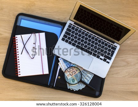 Folder for documents with dollar and Euro bills, Notepad, glasses and laptop on a wooden texture surface top view.