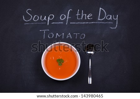 Chalkboard advertising the tomato as soup of the day, with a bowl of tomato soup and spoon, garnished with parsley.