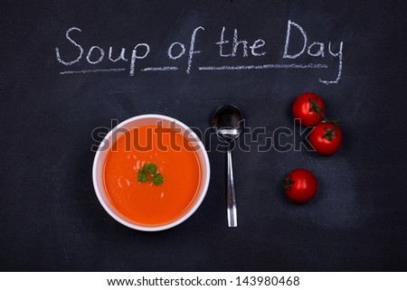 Chalkboard advertising the soup of the day, with a bowl of tomato soup and spoon, garnished with parsley, with  tomatoes on the side