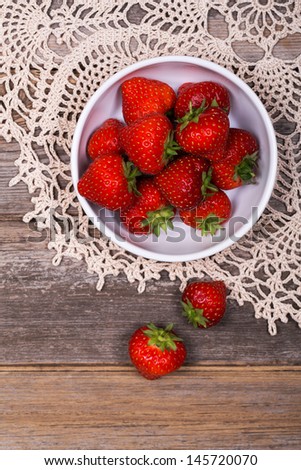 A bowl of fresh ripe strawberries on lace tablecloth and rustic wood table. Vintage effect.