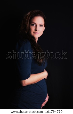 Low key portrait of a happy young woman, in the early stages of pregnancy, showing her enlarging body