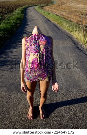 Barefoot woman standing on the asphalt of a country road. She has her head back in the same direction that the road.