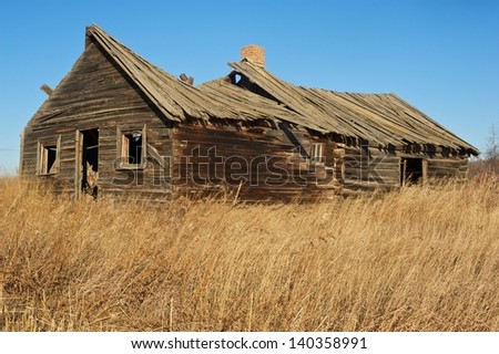 Old abandoned log cabin in dry dead grass in fall