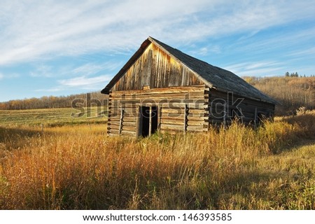 Abandoned log barn on a grassy hillside in fall Trees and harvested fields in the background