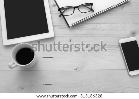 notepad , glasses , notebook , mobile phone and a cup of coffee on table processed with black and white