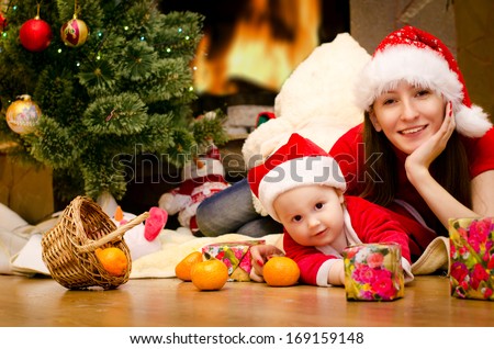 mother and daughter lie under the Christmas tree by the fireplace with a basket of tangerines