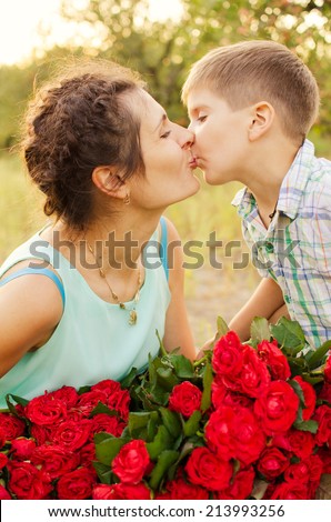 kiss of mom and son, little boy gives his mother a large bouquet of red roses