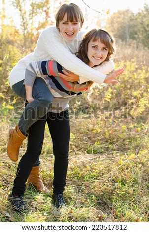 Two girls having fun in the autumn woods climbed on each other\'s backs