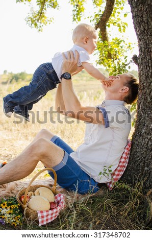 Dad throws up his son at a picnic under a big tree
