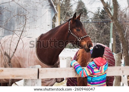 Beautiful girl caressing, taking care her horses at ranch.