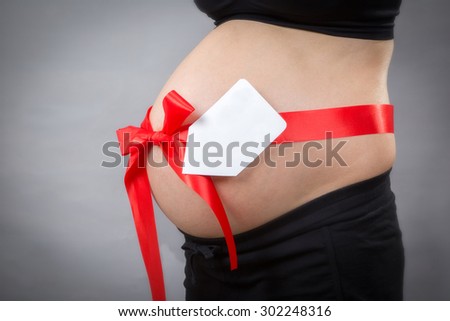 Closed-up of pregnant woman with name tag on tummy at gray background.