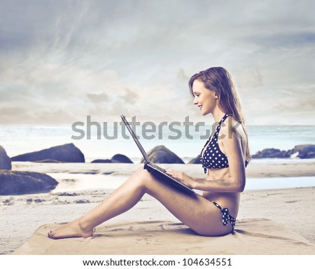 Beautiful woman sitting on a beach and using a laptop
