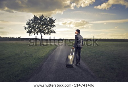 Businessman walking on a long countryside road with a luggage