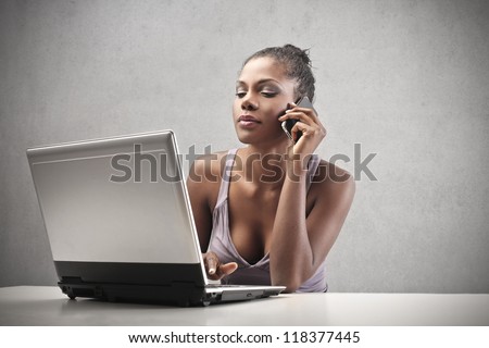 Beautiful black woman using a smart-phone and a laptop computer