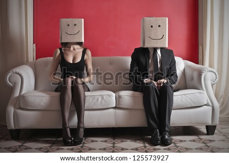 A woman and a man sitting on a sofa with a box on which is drawn a smile over their heads