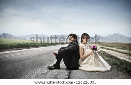 Two newlyweds sitting backs against their backs on a long road