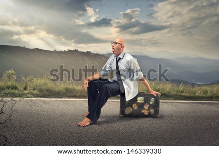 businessman sitting on a suitcase in the middle of the road destroyed by the heat