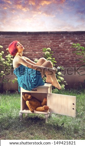 beautiful girl with red hair sitting on top of a piece of furniture in the garden