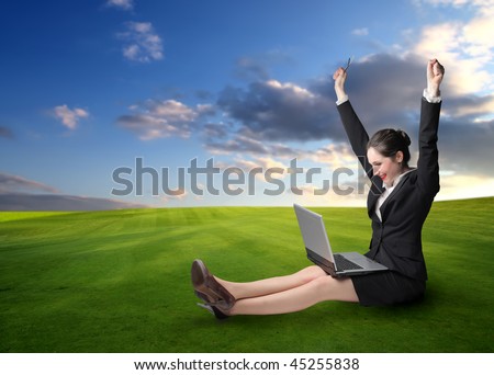 Exulting woman with a laptop on her knees and sitting on the green grass