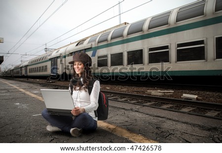 Portrait of a woman sitting on the platform of a train station and working on a laptop