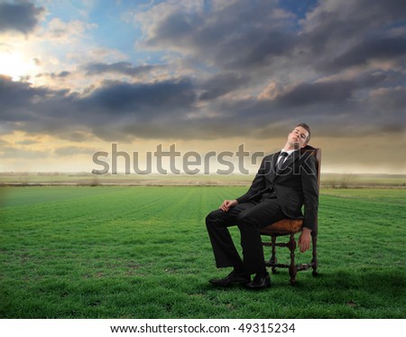 Tired businessman sitting on a chair on a green meadow