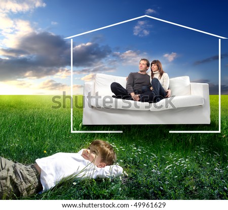 Smiling couple sitting on a couch and happy child lying on green meadow