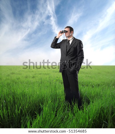 Businessman standing on a green meadow and using binoculars