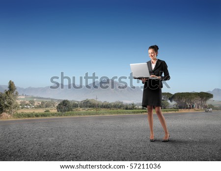 Businesswoman standing on a countryside road and holding a laptop