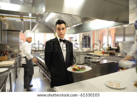 Waiter showing a plate and cook on the background of a restaurant kitchen