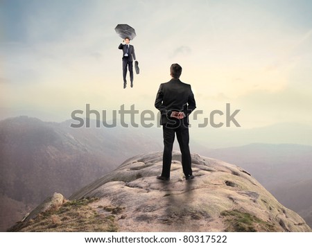 Businessman standing on a peak and observing another businessman flying