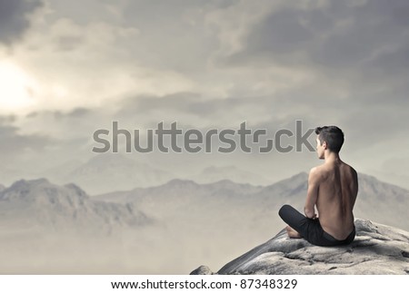 Handsome bare-chested man sitting on a peak over the mountains