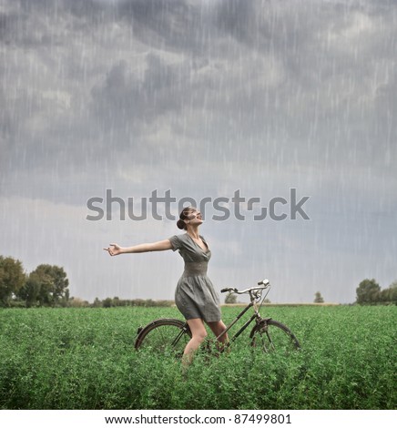 Beautiful woman cycling on a green meadow in the rain